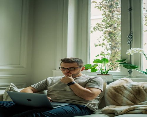 Person working comfortably on a laptop near a large window in an apartment